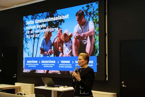 Hyvinvointialuejohtaja Sanna Svahn puhuu mikrofoniin. Hänen takanaan on isolla näytöllä esitysdia, jossa lukee "Jotta länsiuusimaalaiset voivat hyvin."