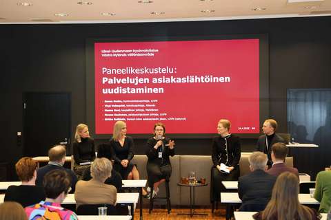 Yleisön edessä istuu paneelikeskustelun vieraita: Attendon toimitusjohtaja Virpi Holmqvist, Mehiläisen kaupallinen johtaja Hanna Hovi ja Länsi-Uudenmaan hyvinvointialueen asiakasohjauksen johtaja Moona Kautonen. Heidän vieressään istuvat hyvinvointialuejohtaja Sanna Svahn ja johtava erityisasiantuntija Nico Vehmas.