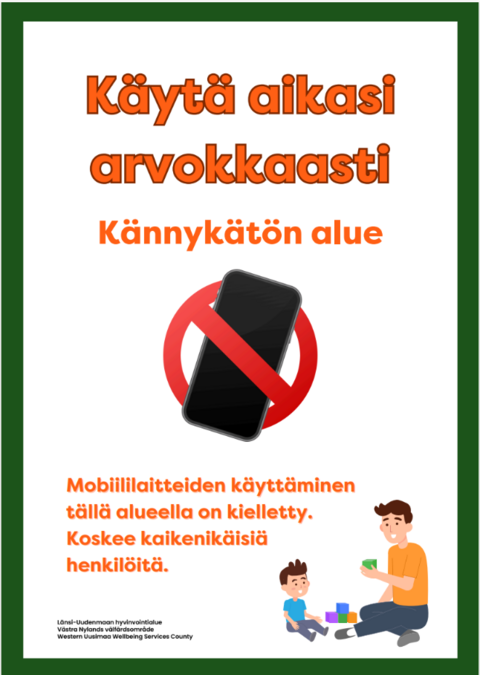 Kuva kyltistä, jossa lukee: "Käytä aikasi arvokkaasti, kännykätön alue. Mobiililaitteiden käyttäminen tällä alueella on kielletty. Koskee kaikenikäisiä henkilöitä." Kuvan alalaidassa piirretty kuva, jossa mies ja lapsi leikkivät palikoilla.