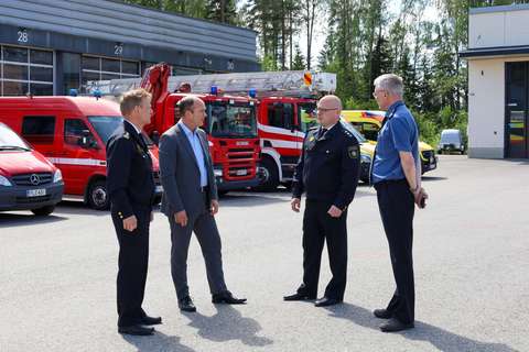 Pelastusjohtaja Veli-Pekka Ihamäki, sisäministeriön kansliapäällikkö Matti Sarasmaa sekä kalustomestari Petteri Ranta ja tekninen päällikkö Jyrki Lehtonen seisovat paloaseman parkkipaikalla. Taustalla on hälytysajoneuvoja.
