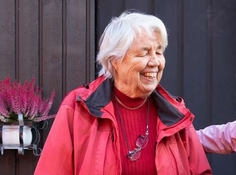 Ikääntynyt hymyilee talonsa edessä.