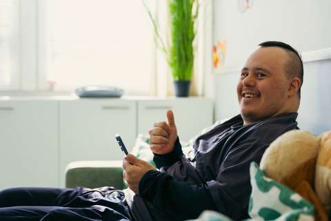 Kännykkää käyttävä mies katsoo kameraan ja näyttää peukkua.