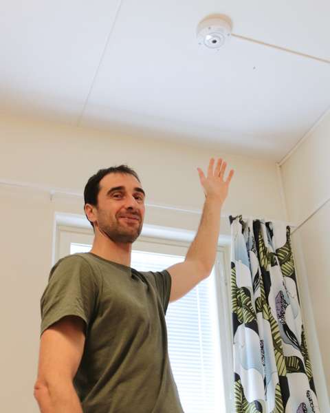 Henkilö esittelee hoivakodin kattoon sijoitettua sensoria. 